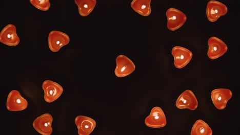 overhead shot of romantic lit heart shaped red candles revolving on black background flickering