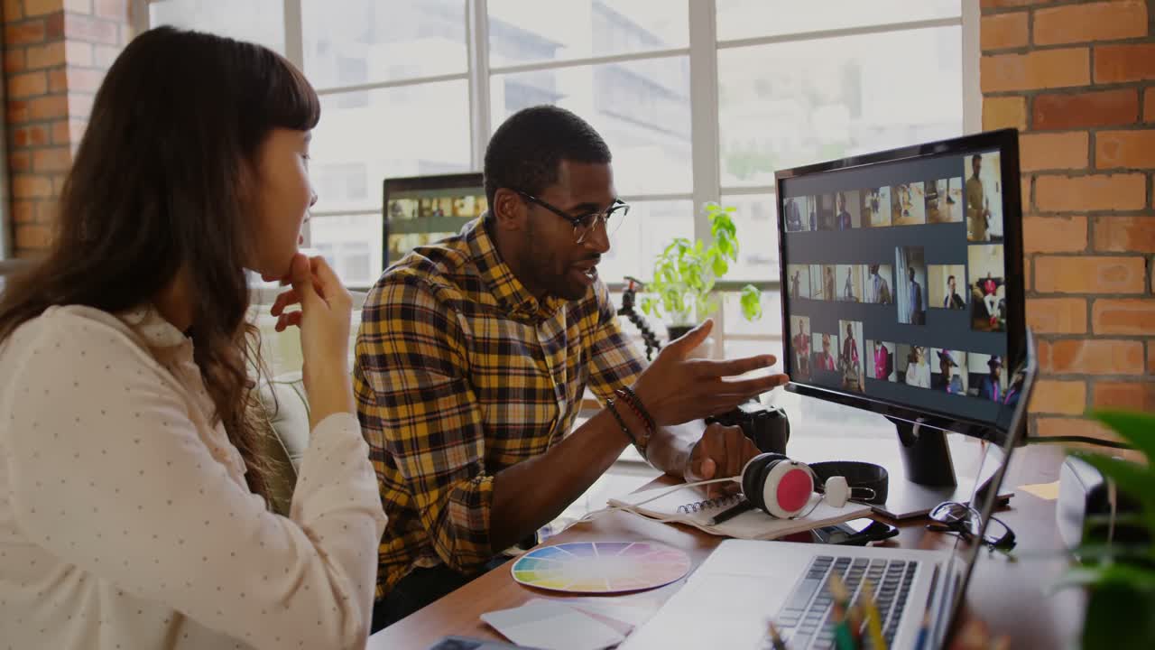 Graphic designers working on photos over computer at desk in office 4k