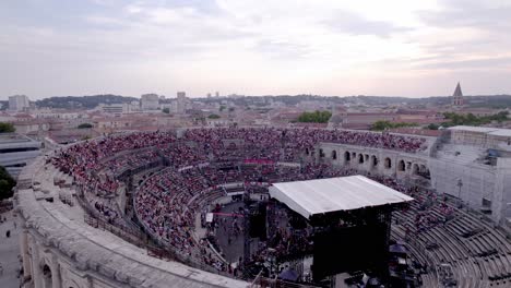 Drone-rotation-over-the-Arena-of-Nimes-at-sunset,-people-are-waiting-for-the-stromae-concert