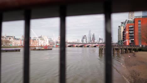 London-City-skyline-view-from-the-river-Thames,-through-a-fence,-in-slow-motion