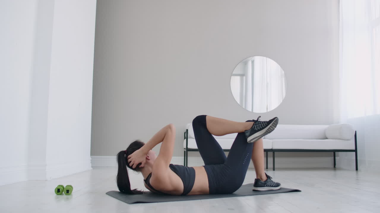 la morena realiza ejercicios musculares abdominales tendida en el suelo y levantando su cuerpo hasta las rodillas.