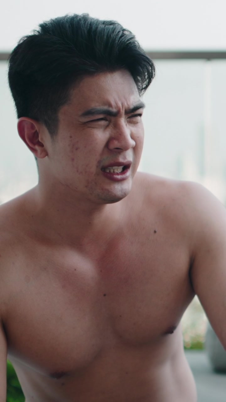 Shirtless Asian Man Holding a Glass of Drink on a Balcony