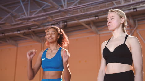 Cheerful-Female-Athlete-Celebrating-Victory-While-Her-Competitor-Looking-At-Her-In-An-Indoor-Sport-Facility