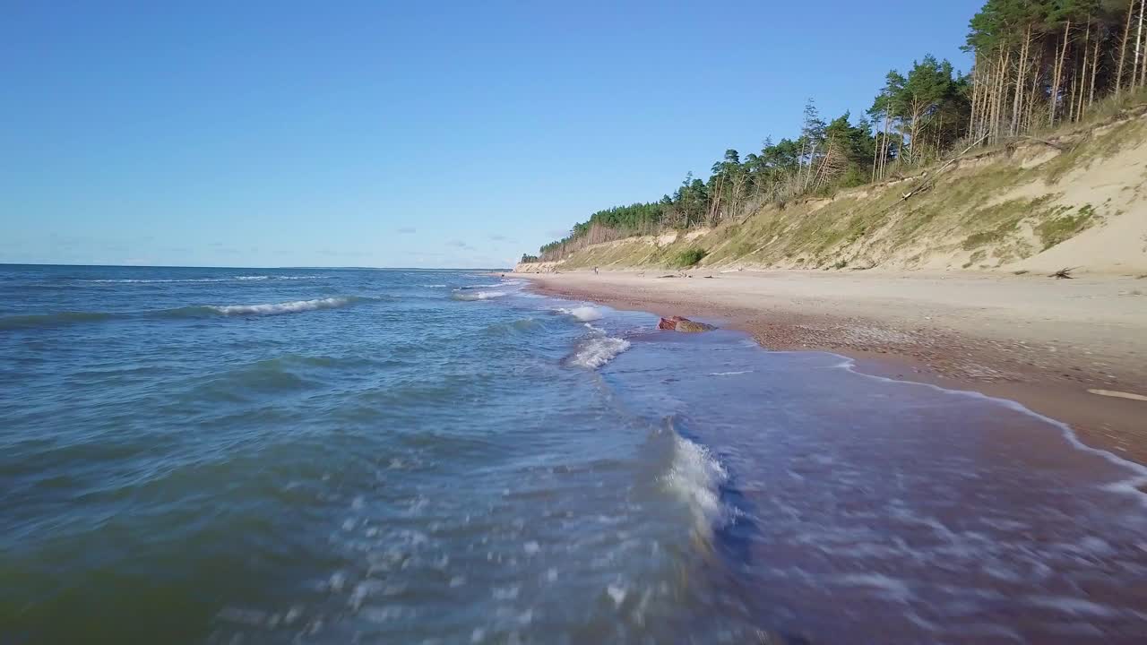 Aerial view of Baltic sea beach at Jurkalne on a sunny day, white sand cliff damaged by waves, coastal erosion, climate changes, wide low angle drone shot moving backwards