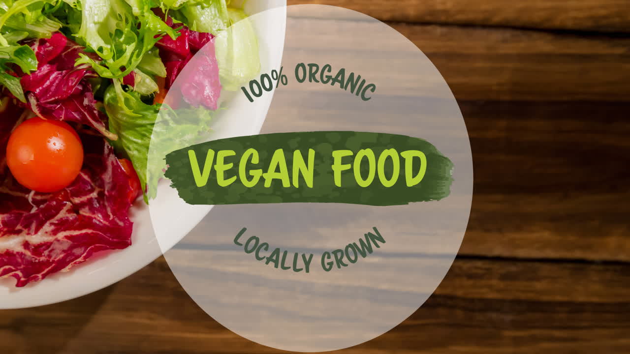 Animation of vegan food text on green over plate of fresh salad on wooden table