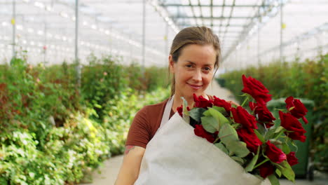 florista femenina alegre con rosas en el invernadero de flores