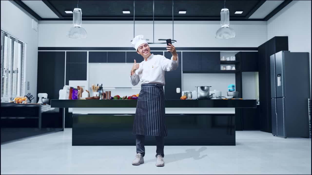 cuerpo lleno de chef asiático usando teléfono inteligente tomando fotos mientras está de pie en la cocina de casa