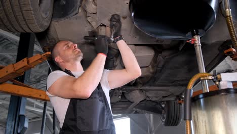 mechanic performing an oil change or other maintenance on a car lifted in a garage