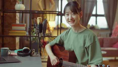 portrait of asian woman with guitar at home recording studio