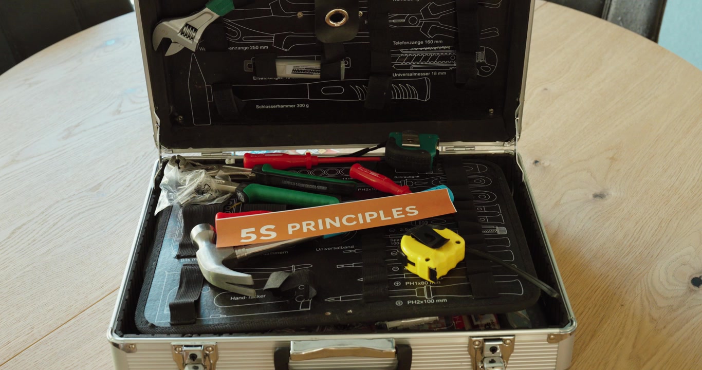 Hand holding “5S Principles” card over a toolbox, representing lean management methods for workplace organization and efficiency.