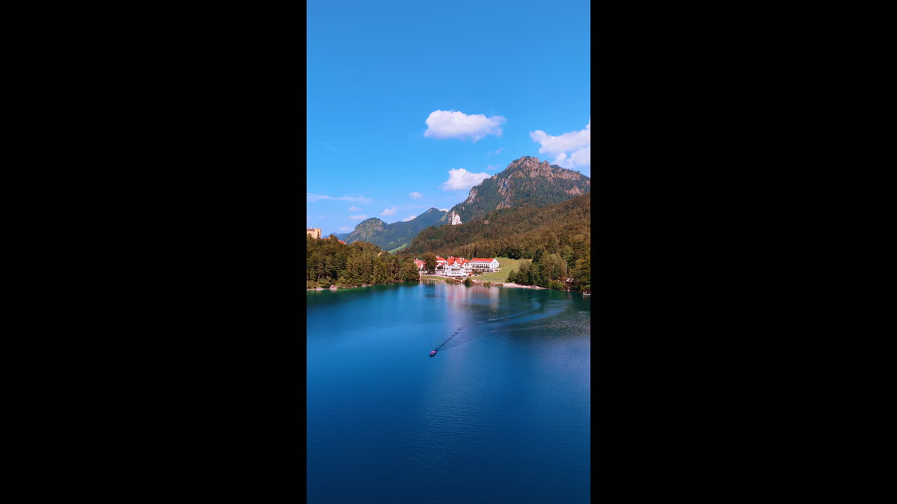 Beautiful lake surrounded by spectacular nature. Boat moves by the waterscape. Neuschwanstein Castle at backdrop. Bavaria, Germany. Vertical video