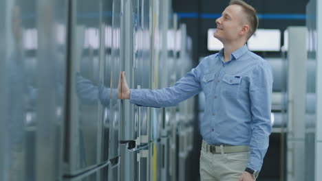 young handsome man chooses a refrigerator for purchase. opens the door and inspects the device, examines the price tags and the characteristics of the model.