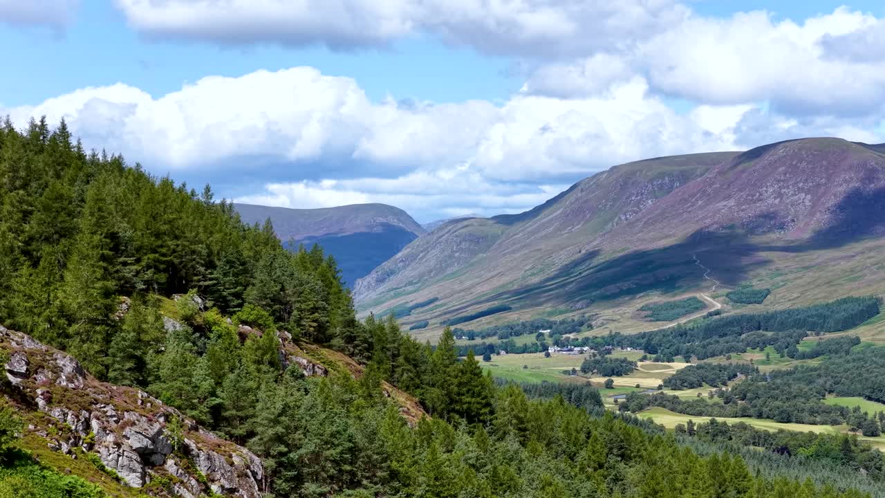 Camera slowly pans over green pine forest, rocky slopes, and expansive Highlands valley under daylight