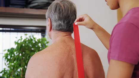 Physiotherapist-sticking-tape-on-senior-patient-back-4k