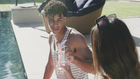 happy biracial couple with drinks at pool in garden on sunny day