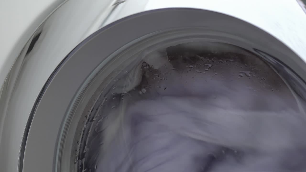 puerta de la máquina de lavar con prendas giratorias en el interior