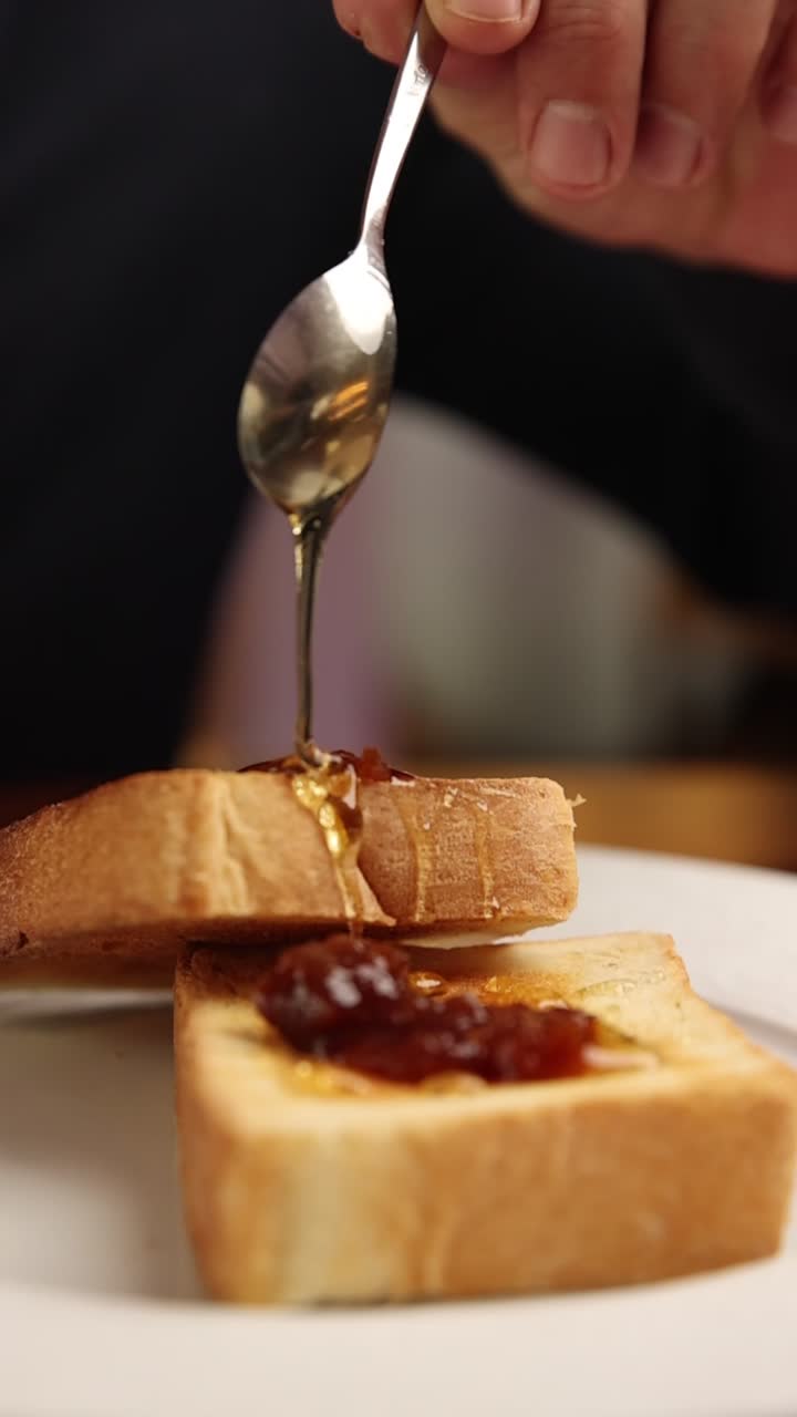 Hand Pouring Golden Honey onto Toasted Bread with Jam