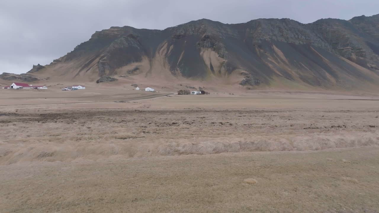 volando sobre hierba y tierra húmeda en el campo de islandia, casas de pueblo y colinas en el fondo, disparo de drones