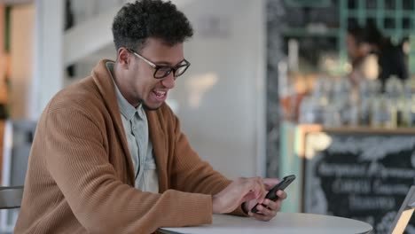 hombre africano celebrando el éxito mientras usa el teléfono inteligente