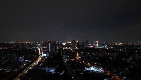 Extra-Lange-Nachtaufnahme-Der-Skyline-Von-Bangkok-Mit-Vielen-Lichtern,-Autos-Und-Zügen-In-4K