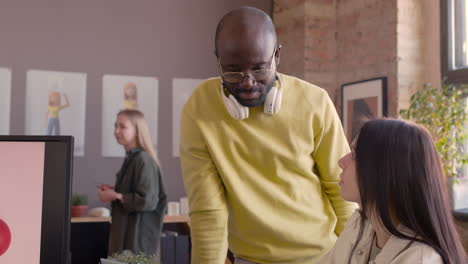 Smiling-Female-Graphic-Designer-Explaining-Project-On-Laptop-Computer-To-Her-Colleague-In-An-Animation-Studio