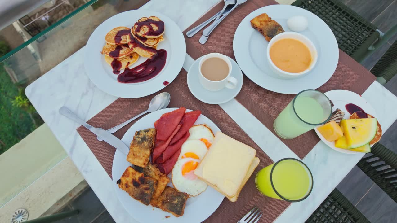 Ovenfra-bilde av kontinental frokost med kaffe, juice, egg og pannekaker på bordet.