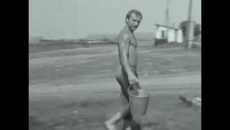 man walking on field holding two buckets. circa ussr 1980s: a man from the soviet union walks on the field, holding two buckets.