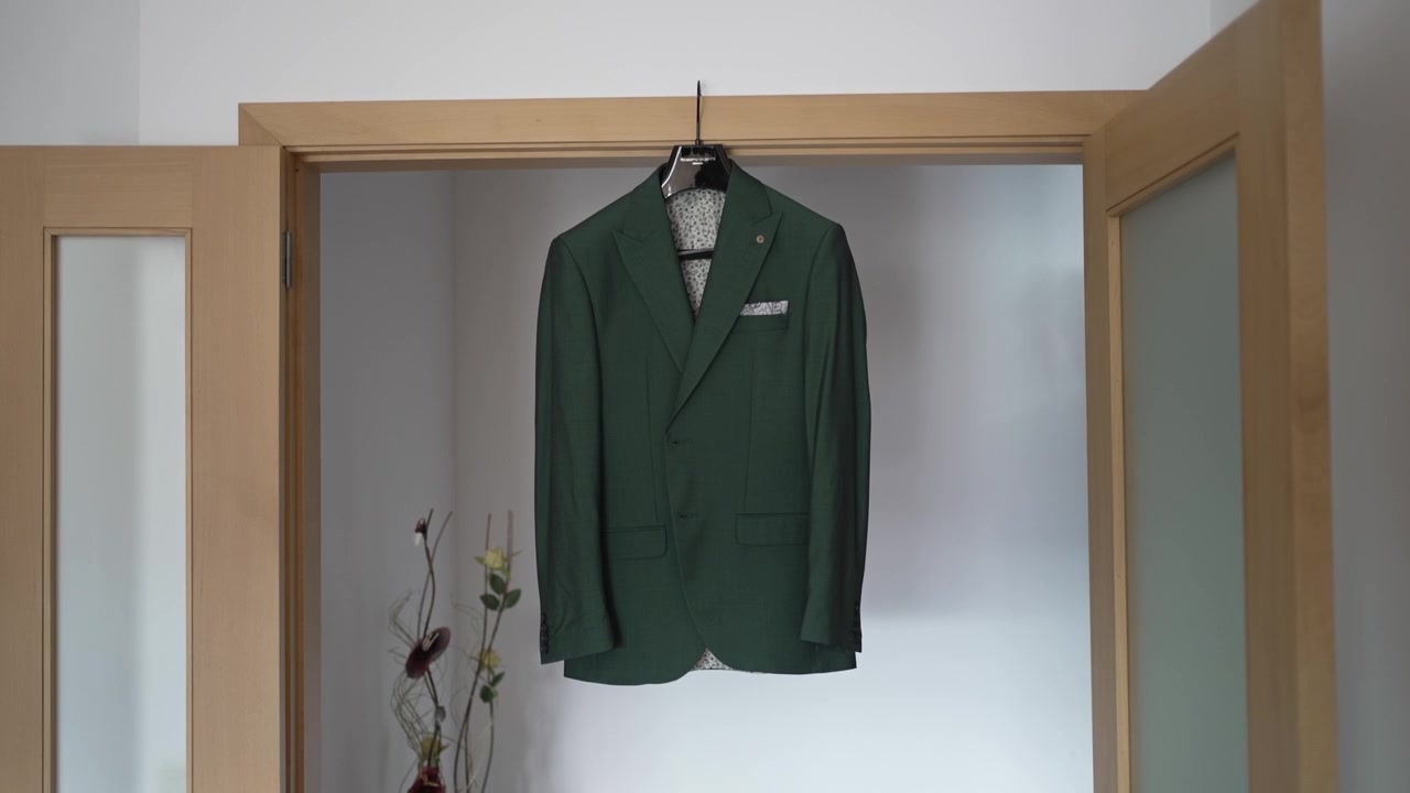 Giacca da completo verde appesa ordinatamente a una gruccia, esposta in un vano porta aperto