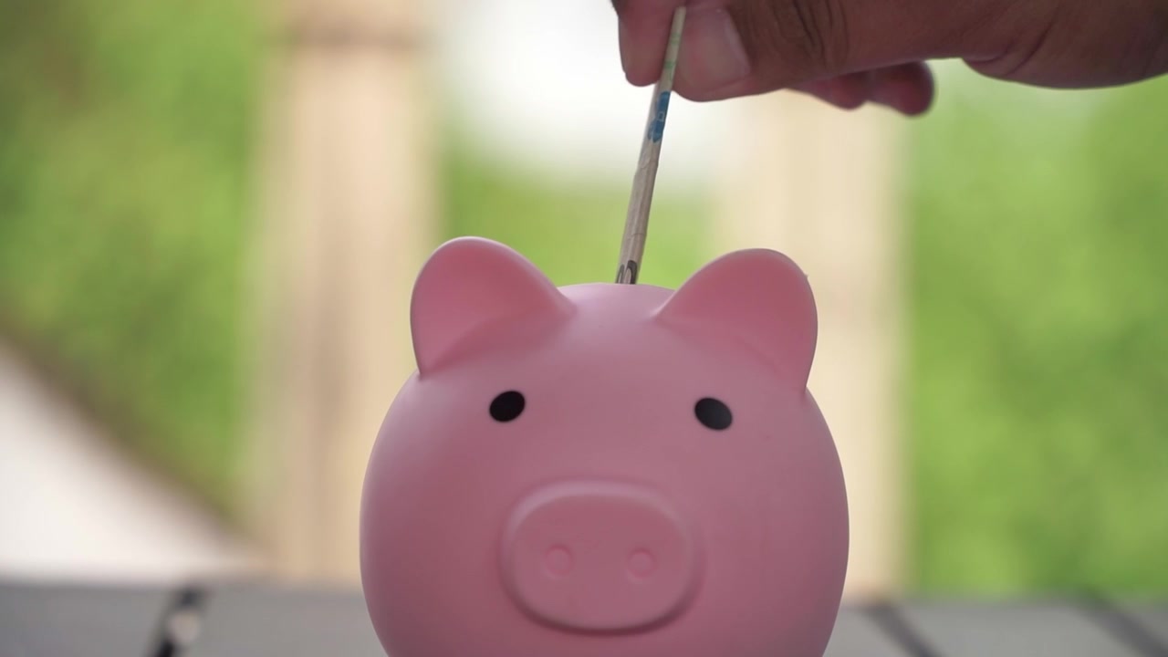 Cofrinho e moedas sobre a mesa, conceito de planejamento financeiro e estratégia de poupança inteligente. Pessoa colocando dinheiro no cofrinho.