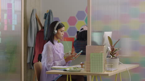 beautiful young mixed race woman student using computer brainstorming working on creative project enjoying study in colorful modern office listening to music wearing headphones