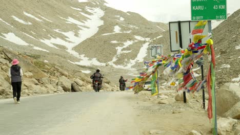 biker drives along road with snow in mountains in ladakh, india, epic peaks and rugged terrain define this high-altitude adventure as buddhist prayer flags flutter in wind