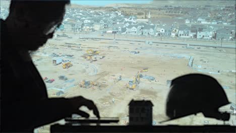 engineer, architect or construction foreman works on the details as heavy equipment gets the building site ready in the background