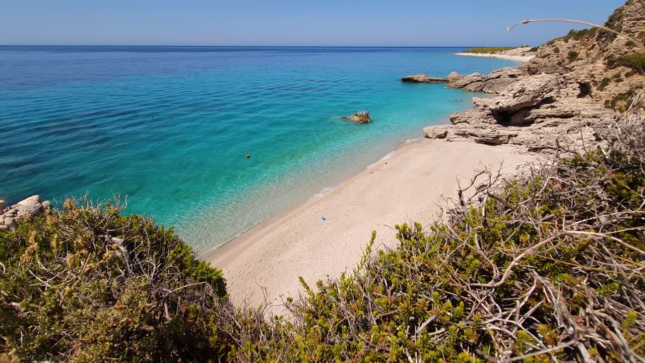 Paradise beach with white sand sheltered by rocks and wild flowers, washed by blue turquoise sea water, idyllic summer vacation spot in Mediterranean