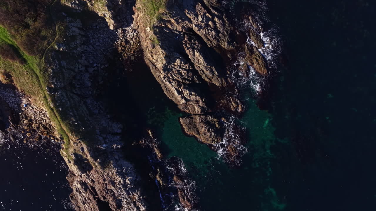 Scogliere costiere incontrano il mare vivace, mentre le onde si infrangono in modo spettacolare contro le rocce frastagliate sotto la luce del sole.