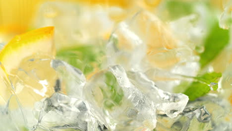 making lemonade by pouring soda water over ice cubes, lemon slices and mint in macro and slow motion