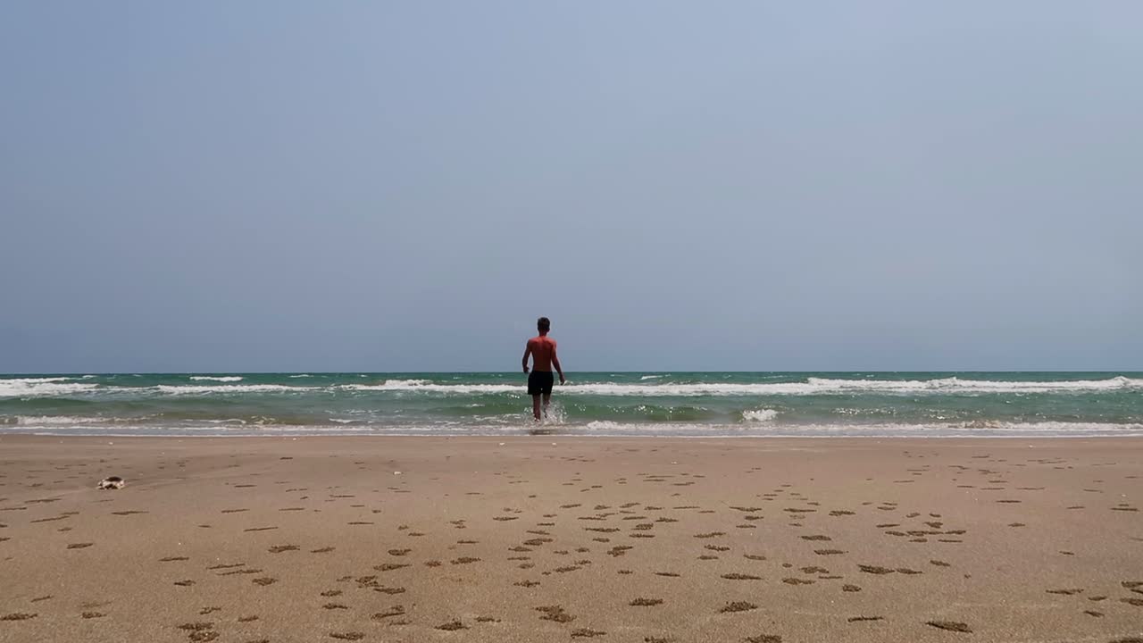 imágenes de 4k de un hombre solitario en forma que camina casualmente en una playa vacía y se sumerge en el océano
