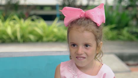 young-lady-with-huge-purple-bow-smiles-against-swimming-pool