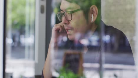 asian man wearing wireless earphones having a video call on laptop while sitting at a cafe