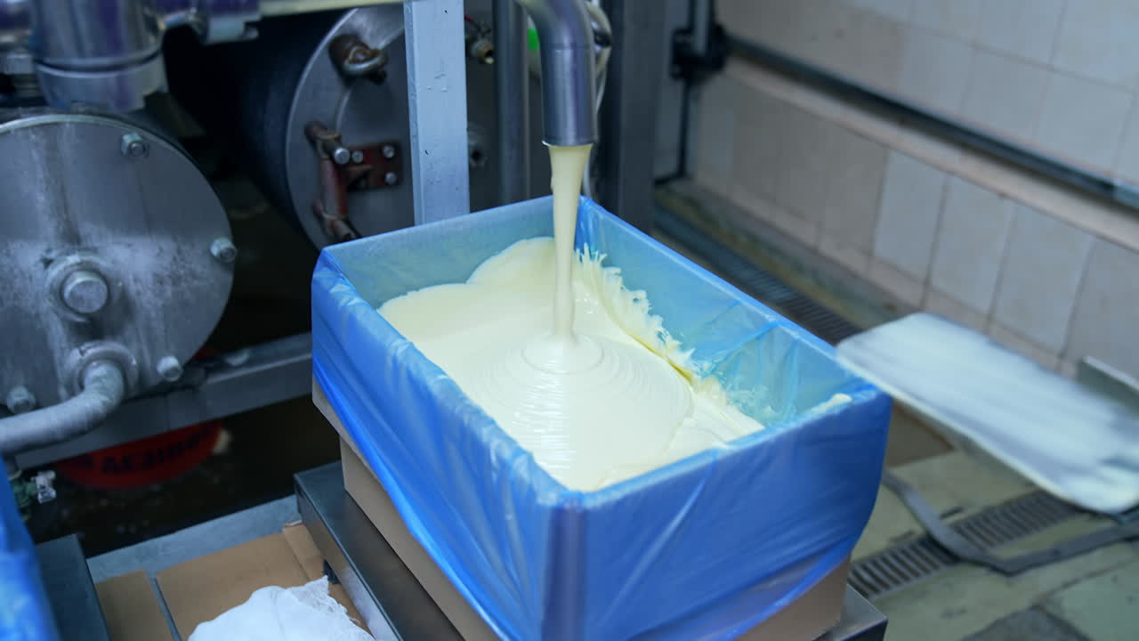 Liquid butter is pouring from the pipe into the container. Factory for the production of butter. Automated line. Food production.