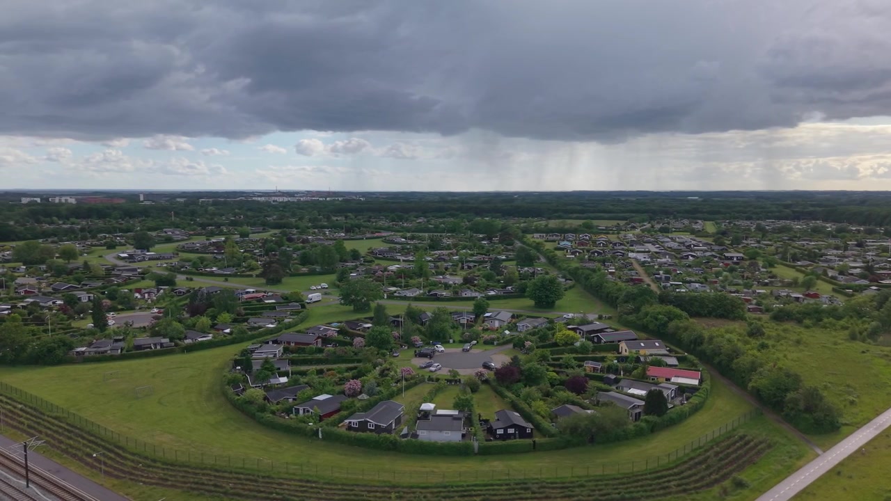 Riprese aeree con drone che sorvolano Haveforeningen Harekaer, rivelando la sua notevole disposizione circolare incorniciata da una vegetazione lussureggiante e un cielo drammaticamente coperto sul paesaggio danese