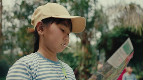 young girl reading a map while eating a lollipop in a park