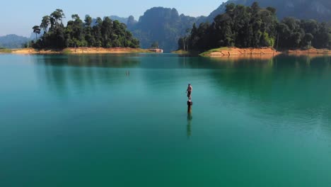 a man standing on a wooden stump, about to jump into the turquoise water of thailand - aerial