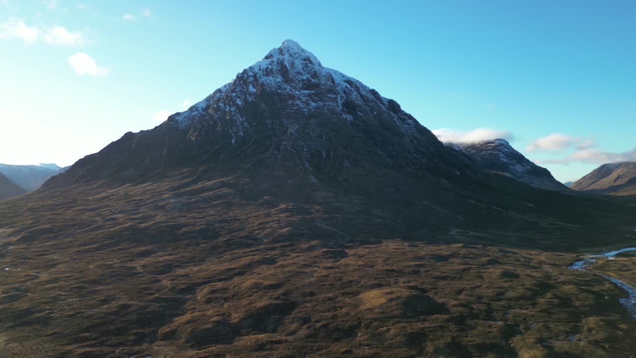Snow-capped mountain peak in Glencoe with blue skies, aerial view