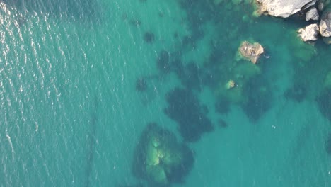 Top-down-aerial-over-idyllic-blue-water-of-Ionian-Sea-and-coast-of-Parga,-Greece