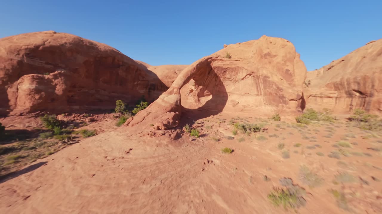 An FPV drone circling under the red sandstone Funnel Arch in the sandy and rocky desert of Moab Utah
