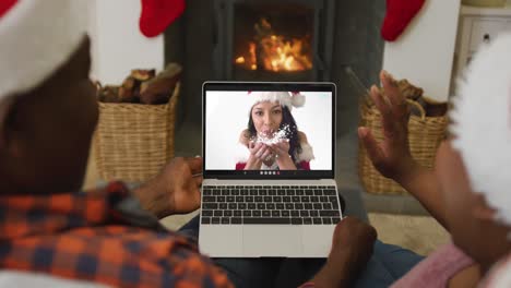 Afroamerikanisches-Paar-Mit-Weihnachtsmützen-Nutzt-Laptop-Für-Weihnachtsvideoanruf-Mit-Frau-Auf-Dem-Bildschirm