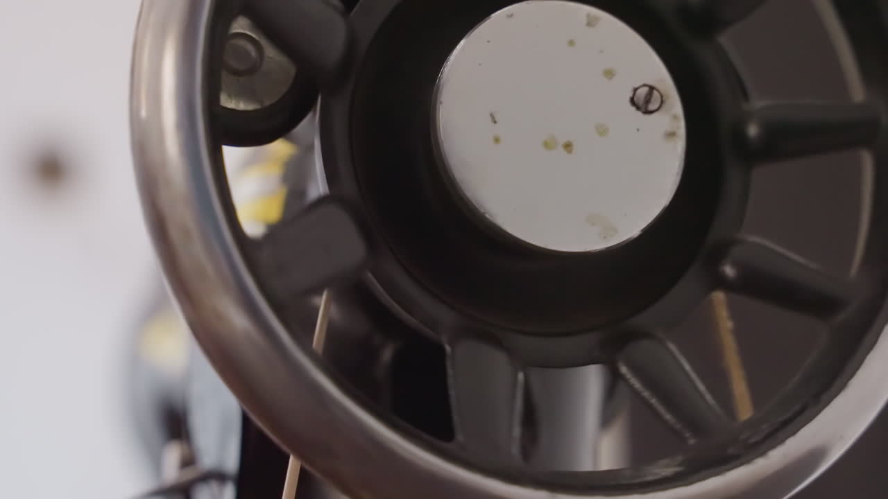 Inspección de cerca de máquina de coser negra para tareas domésticas, técnico ajustando cubo corroído, placa manchada y suciedad, ajuste de precisión, ambiente de banco de taller, narrativa de reparación práctica.