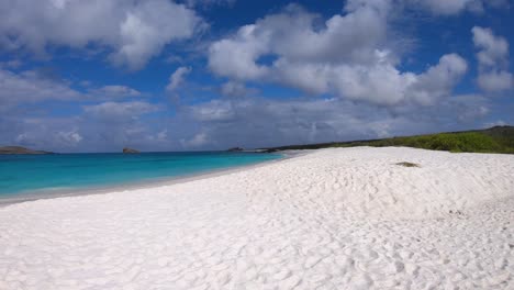 white sand beach of the galapagos islands with clear turquoise water. on the back some small islands can be seen.