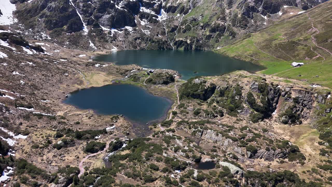 The Murgsee region of Switzerland displays high alpine scenery with deep blue lakes, snow patches on rugged peaks, and open green valleys where mountain cabins rest below a bright summer sky