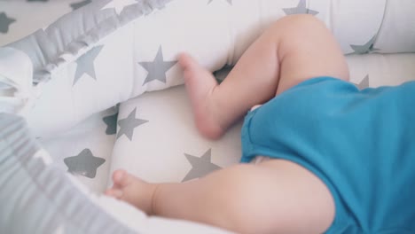 un niño pequeño en traje de cuerpo yace molestando las piernas desnudas en el capullo